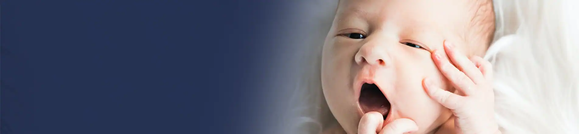A newborn baby yawns with tiny hands near its face