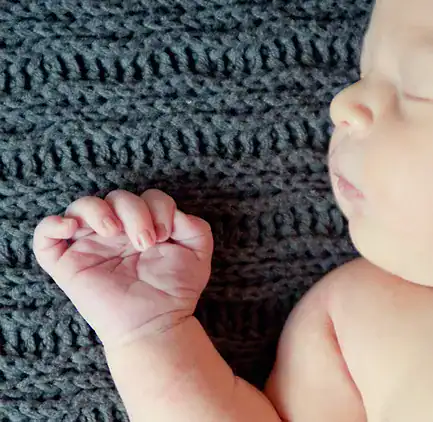 A sleeping baby on a dark knitted blanket