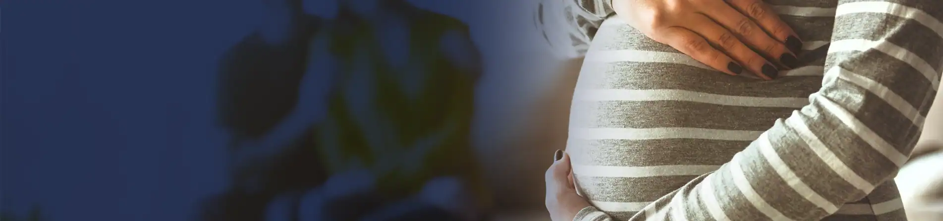 Pregnant person in a striped shirt gently cradling their belly